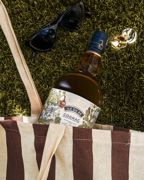 A high-quality lifestyle photograph featuring a bottle of Cognac placed in a casual, outdoor setting with sunglasses and jewelry.